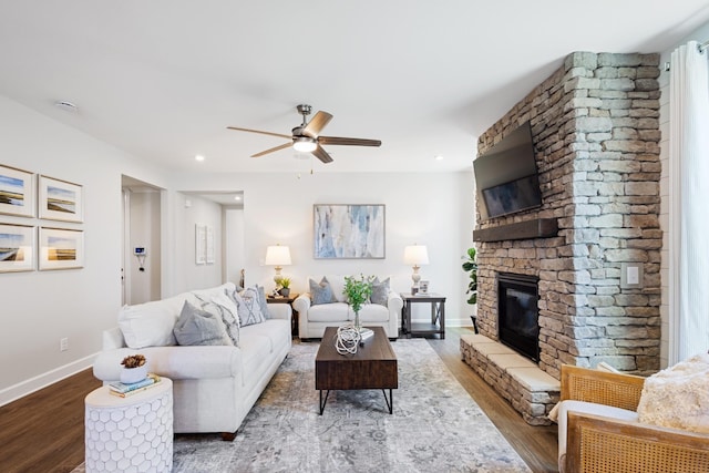 living room featuring a stone fireplace, dark wood-type flooring, and ceiling fan