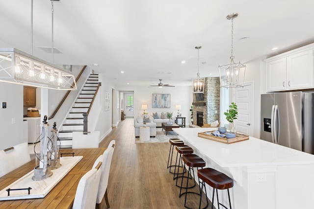 kitchen featuring a breakfast bar, a fireplace, decorative light fixtures, white cabinets, and stainless steel refrigerator with ice dispenser