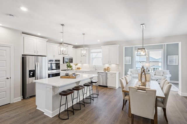 kitchen featuring a kitchen island, white cabinets, backsplash, hanging light fixtures, and stainless steel appliances