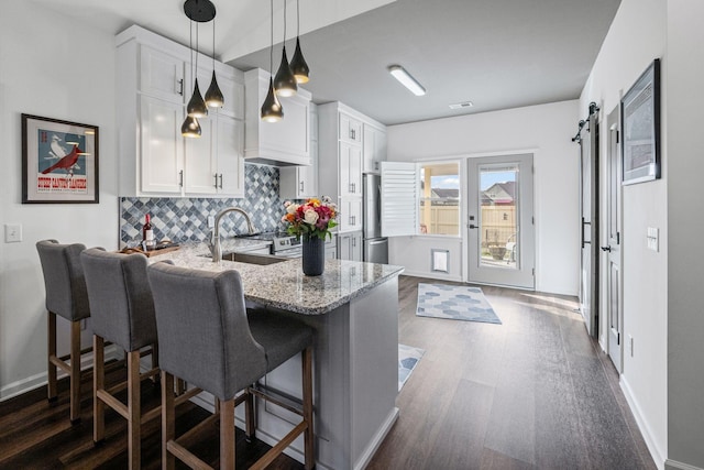 kitchen featuring a breakfast bar, sink, white cabinetry, kitchen peninsula, and a barn door