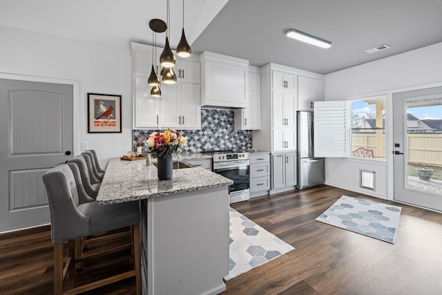 kitchen with pendant lighting, appliances with stainless steel finishes, a kitchen breakfast bar, light stone countertops, and white cabinets