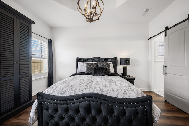 bedroom with dark hardwood / wood-style floors, a barn door, and a chandelier