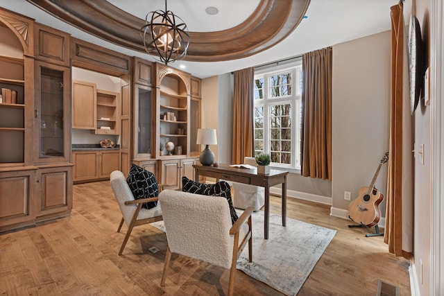 office space with an inviting chandelier, a tray ceiling, and light wood-type flooring