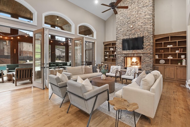 living room featuring a fireplace, a high ceiling, ceiling fan, light hardwood / wood-style floors, and french doors