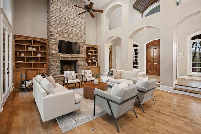 living room featuring a stone fireplace, built in features, and light wood-type flooring