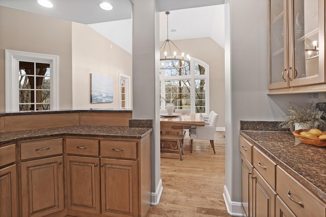 kitchen featuring vaulted ceiling, light hardwood / wood-style flooring, dark stone countertops, a notable chandelier, and pendant lighting