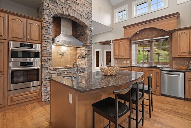 kitchen with sink, a breakfast bar area, appliances with stainless steel finishes, a kitchen island with sink, and wall chimney range hood