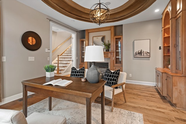 office space featuring an inviting chandelier, a tray ceiling, and light hardwood / wood-style floors