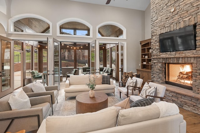 living room with a stone fireplace, a towering ceiling, hardwood / wood-style flooring, ceiling fan, and french doors