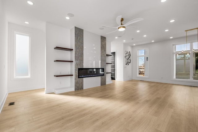 unfurnished living room featuring a large fireplace, ceiling fan, and light hardwood / wood-style flooring