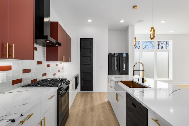 kitchen with pendant lighting, sink, black appliances, light wood-type flooring, and wall chimney exhaust hood