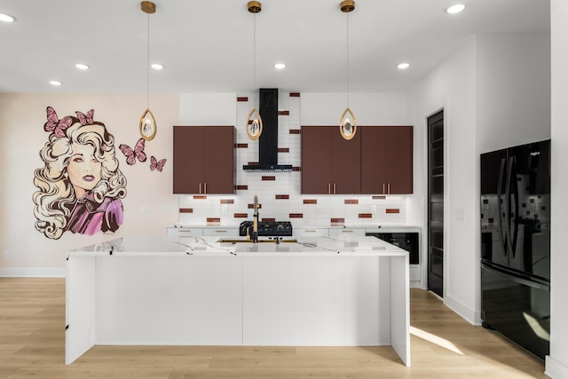 kitchen featuring black refrigerator, backsplash, decorative light fixtures, and wall chimney exhaust hood