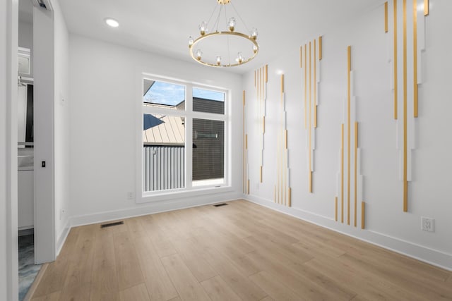 unfurnished room featuring a chandelier and light hardwood / wood-style flooring