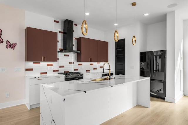 kitchen with decorative light fixtures, an island with sink, sink, black appliances, and wall chimney range hood