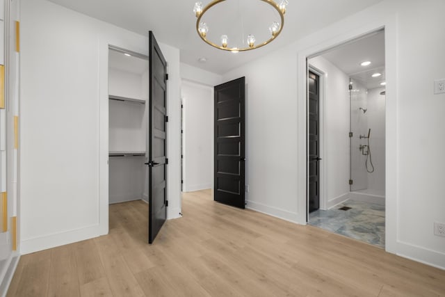 unfurnished bedroom featuring light hardwood / wood-style flooring, a chandelier, a walk in closet, ensuite bath, and a closet