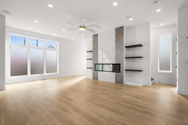 unfurnished living room with ceiling fan, a fireplace, and light hardwood / wood-style floors