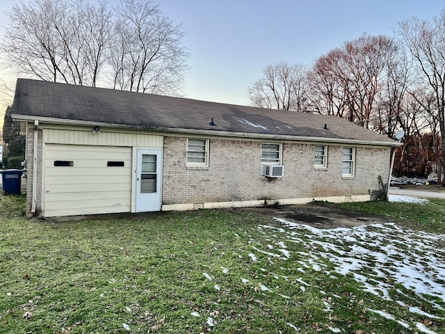 snow covered rear of property with cooling unit, a garage, and a lawn