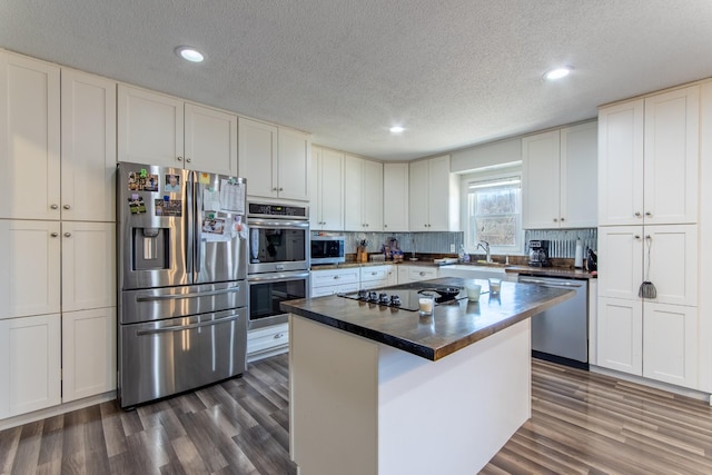 kitchen featuring sink, dark wood-type flooring, stainless steel appliances, a center island, and white cabinets