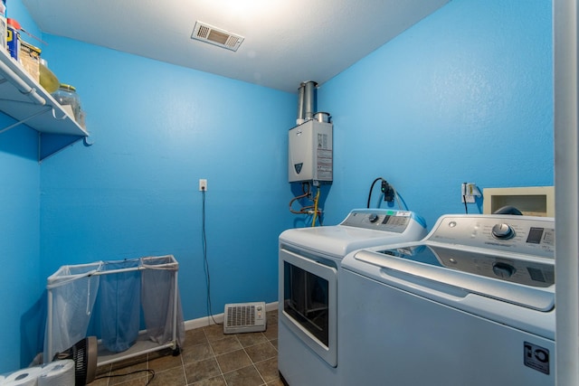 clothes washing area featuring washing machine and clothes dryer, tankless water heater, and dark tile patterned flooring