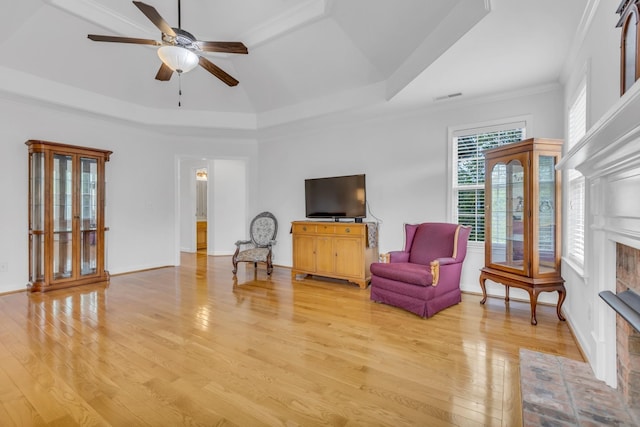 living area with a brick fireplace, a tray ceiling, light hardwood / wood-style floors, and ceiling fan