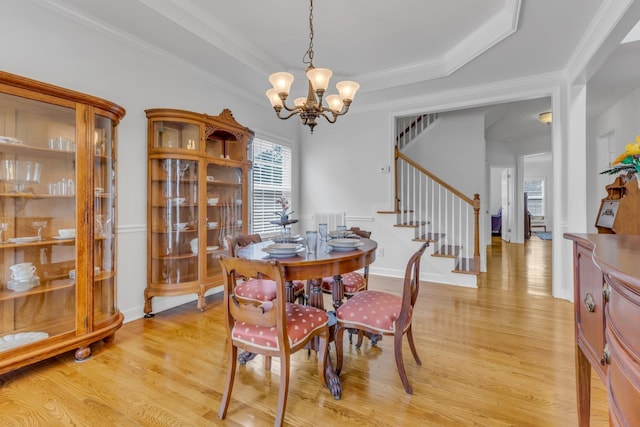 dining area featuring a chandelier, crown molding, a raised ceiling, and light hardwood / wood-style flooring