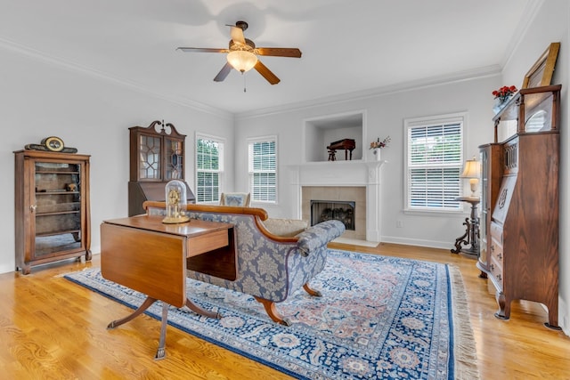 living room with a tiled fireplace, crown molding, ceiling fan, and light wood-type flooring