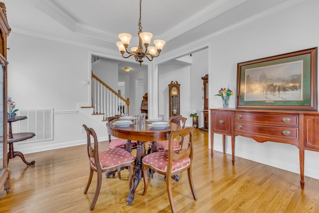 dining space with crown molding, a chandelier, light hardwood / wood-style floors, and a raised ceiling