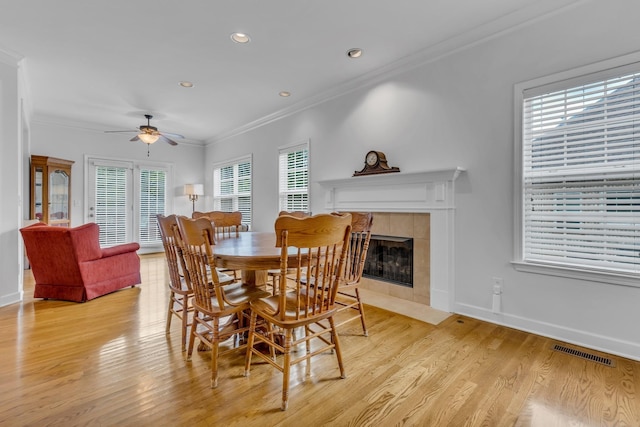 dining room featuring light hardwood / wood-style flooring, a fireplace, ornamental molding, and ceiling fan