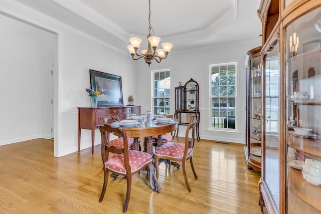 dining space featuring crown molding, a raised ceiling, light hardwood / wood-style floors, and a notable chandelier