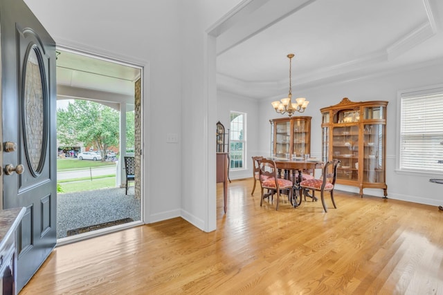 foyer entrance with crown molding, a tray ceiling, a chandelier, and light hardwood / wood-style floors