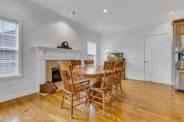 dining area featuring ornamental molding, light hardwood / wood-style floors, and a tile fireplace