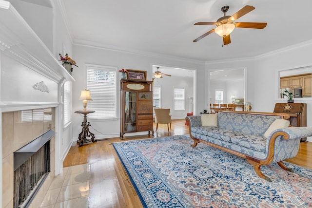 living room with ceiling fan, ornamental molding, a fireplace, and light hardwood / wood-style flooring