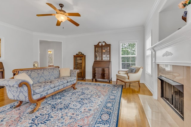 living room featuring crown molding, a tile fireplace, light hardwood / wood-style floors, and ceiling fan