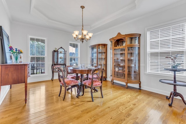 dining space featuring a raised ceiling, crown molding, a chandelier, and light hardwood / wood-style flooring