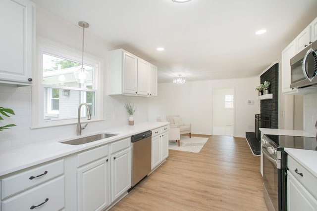 kitchen featuring appliances with stainless steel finishes, decorative light fixtures, white cabinetry, sink, and light hardwood / wood-style floors