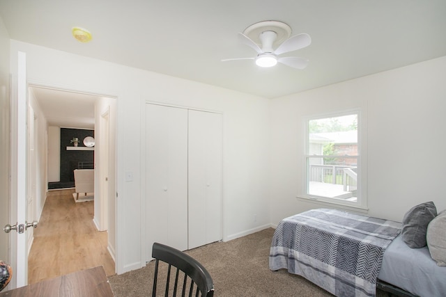 bedroom with a brick fireplace, light colored carpet, a closet, and ceiling fan