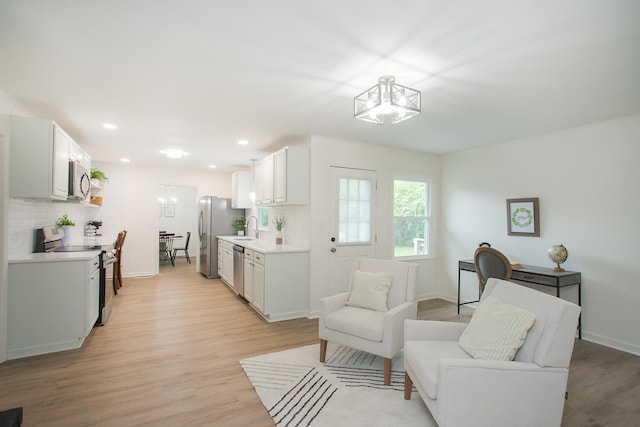 kitchen with appliances with stainless steel finishes, sink, decorative backsplash, and light wood-type flooring