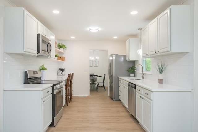 kitchen with sink, light hardwood / wood-style flooring, appliances with stainless steel finishes, hanging light fixtures, and white cabinets