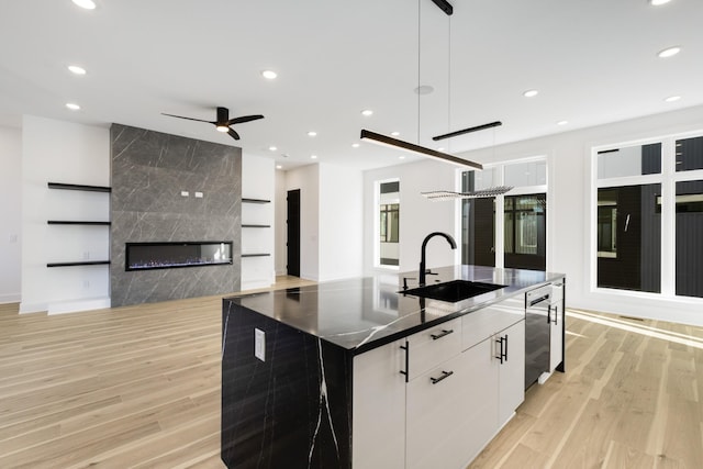 kitchen featuring pendant lighting, sink, white cabinets, stainless steel dishwasher, and a large island with sink