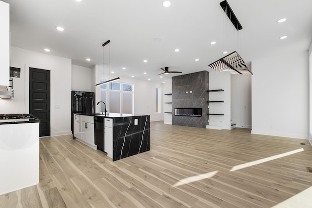 kitchen with a high end fireplace, a kitchen island with sink, hanging light fixtures, and white cabinets