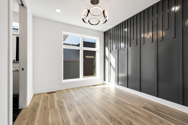 unfurnished room featuring a chandelier and light wood-type flooring