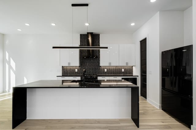 kitchen with an island with sink, white cabinets, hanging light fixtures, black fridge with ice dispenser, and light hardwood / wood-style flooring