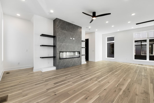 unfurnished living room with ceiling fan, a tile fireplace, and light wood-type flooring