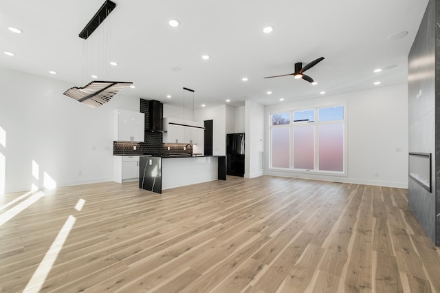 unfurnished living room with ceiling fan, sink, a fireplace, and light hardwood / wood-style floors