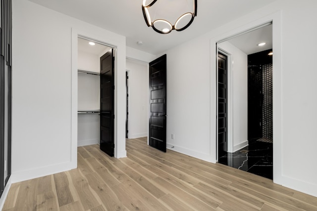 unfurnished bedroom featuring an inviting chandelier, a spacious closet, light hardwood / wood-style floors, and a closet