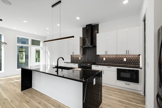 kitchen featuring pendant lighting, sink, a kitchen island with sink, white cabinetry, and wall chimney exhaust hood