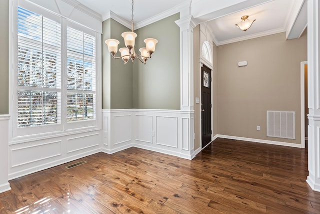 unfurnished dining area with ornate columns, crown molding, dark wood-type flooring, and an inviting chandelier