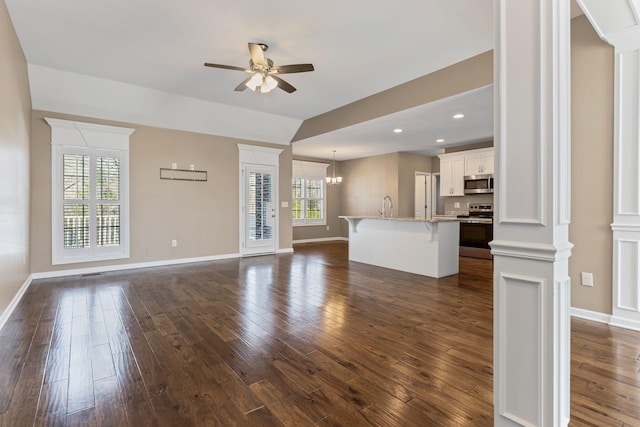 unfurnished living room with ceiling fan with notable chandelier, lofted ceiling, dark hardwood / wood-style floors, and decorative columns