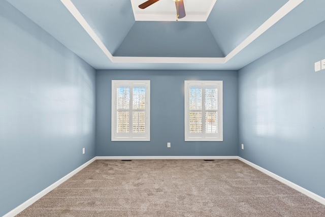 carpeted empty room with a raised ceiling, vaulted ceiling, and ceiling fan