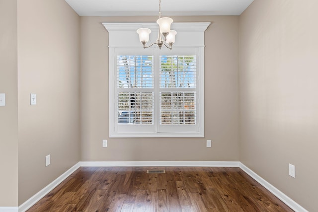 unfurnished dining area featuring dark wood-type flooring and an inviting chandelier